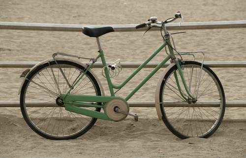 Foto groot bekijken: Groene fiets op het zand bij de boulevard