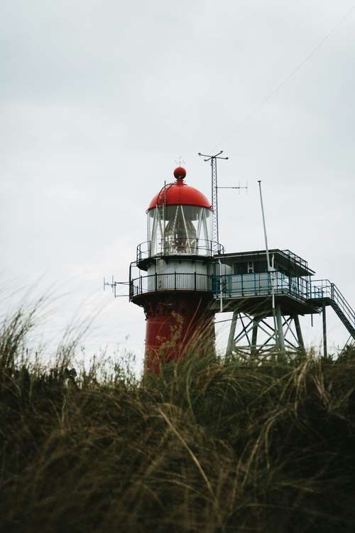 Foto groot bekijken: Rood-witte vuurtoren achter hoog gras